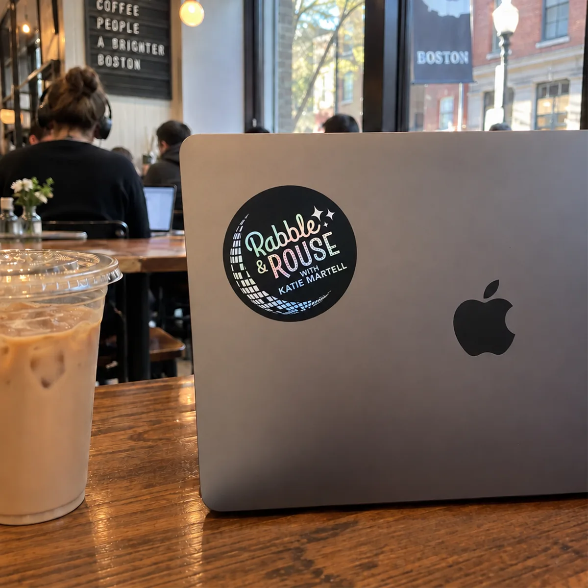 A holographic Rabble and Rouse sticker on a laptop in a Boston coffee shop